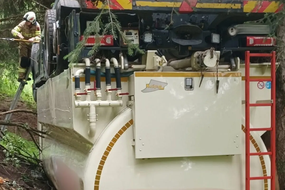 Ein Feuerwehrmann steht auf einer Leiter und untersucht ein auf der Seite liegendes Tankfahrzeug, das im Wald verunfallte. Äste und Pflanzen verdecken Teile des Fahrzeugs.