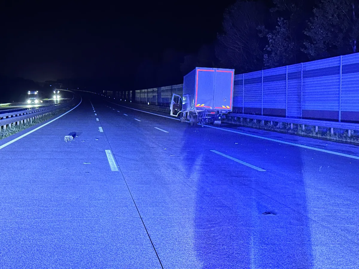 Ein Lastwagen liegt quer zur Fahrbahn auf der Autobahn in der Nacht, eine Schutzwand ist im Hintergrund sichtbar.