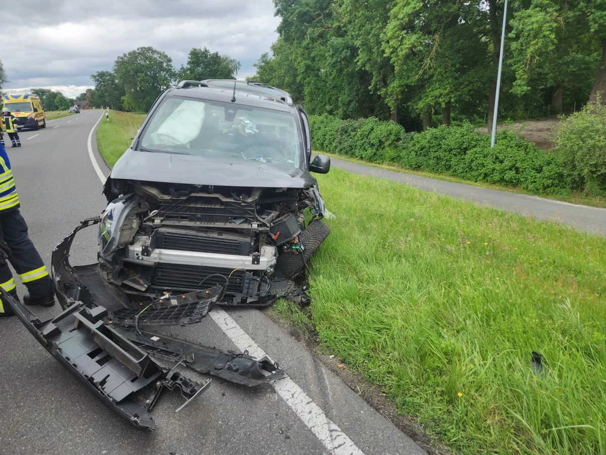 Ein schwarzes Auto mit schwer beschädigter Front steht auf einem Asphaltstreifen neben einer grünen Wiese.