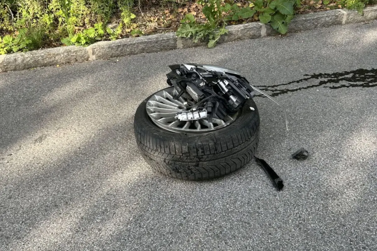 Ein Autoreifen mit beschädigten Autoteilen liegt auf der Straße, umgeben von Trümmern und Spuren auf dem Asphalt.