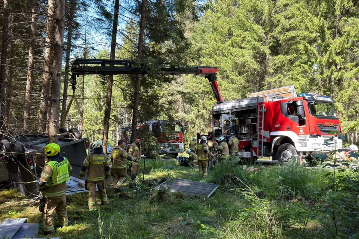 Feuerwehrleute sind in einem Wald, um ein verunglücktes Auto mit einem Hebekran zu bergen. Mehrere Einsatzkräfte sind vor Ort und das Fahrzeug liegt auf dem Dach.