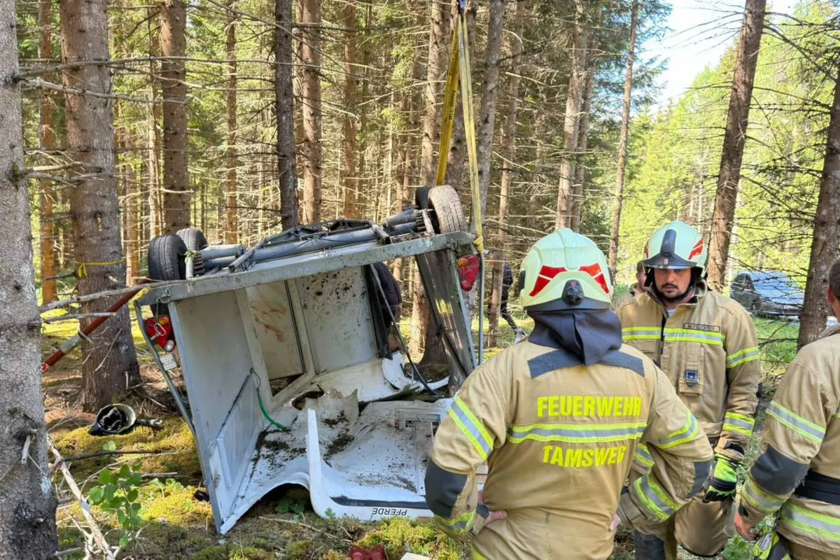 Mehrere Feuerwehrleute stehen neben einem auf dem Dach liegenden Fahrzeug im Wald. Das Fahrzeug zeigt starke Verschmutzungen und Beschädigungen.
