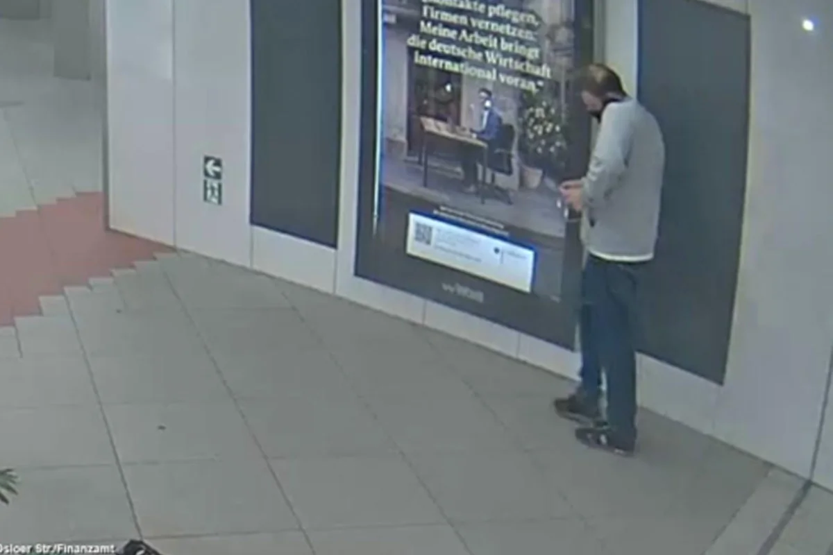 Ein Mann steht in einem Gebäude vor einer großen Werbetafel. Der Boden ist mit Fliesen bedeckt.