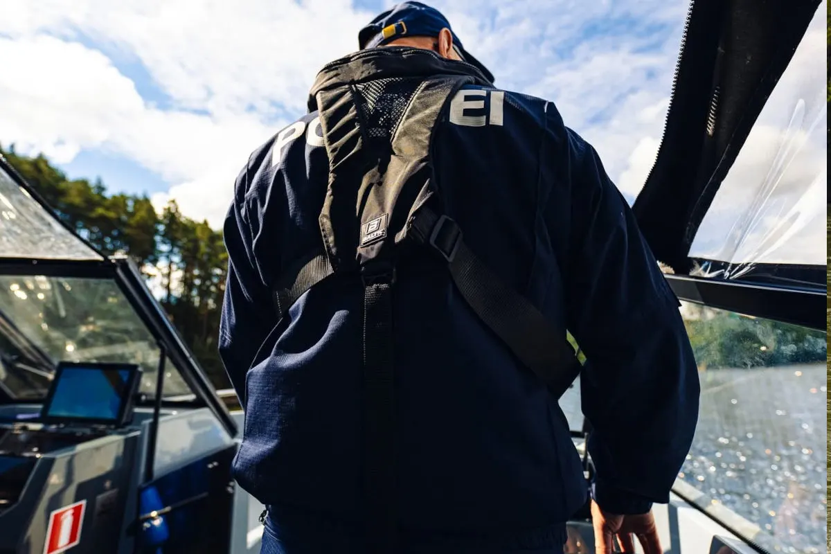 Ein Polizist in blauer Uniform steht auf einem Boot, das sich auf einem Gewässer befindet. Der Himmel ist teilweise bewölkt.