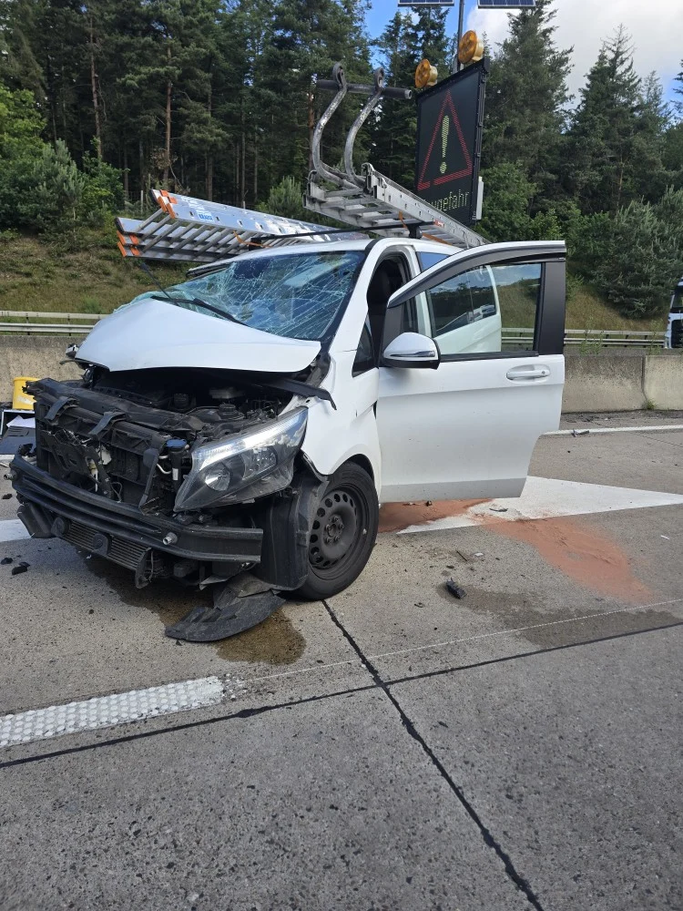 Ein weißes Auto mit stark beschädigter Front steht auf einer Autobahnspur. Ein Verkehrsschild ist im Hintergrund sichtbar.