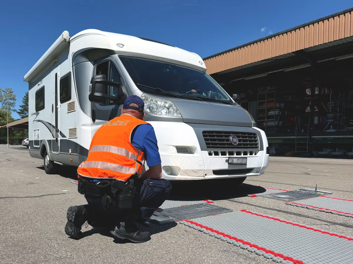 Ein weißes Wohnmobil steht auf einer mobilen Waage. Ein Polizist in orangener Weste kniet neben der Waage.
