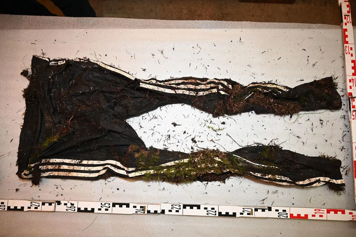 Auf einem Tisch liegt eine verschmutzte und beschädigte schwarze Hose mit weißen Streifen. Verschiedene Markierungen sind sichtbar.