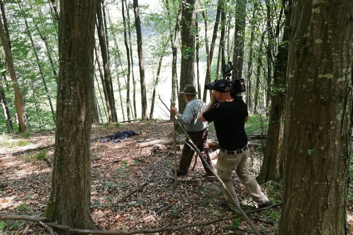 In einem dichten Wald filmt ein Kameramann eine Person, die etwas zu Boden Gefallenes begutachtet.