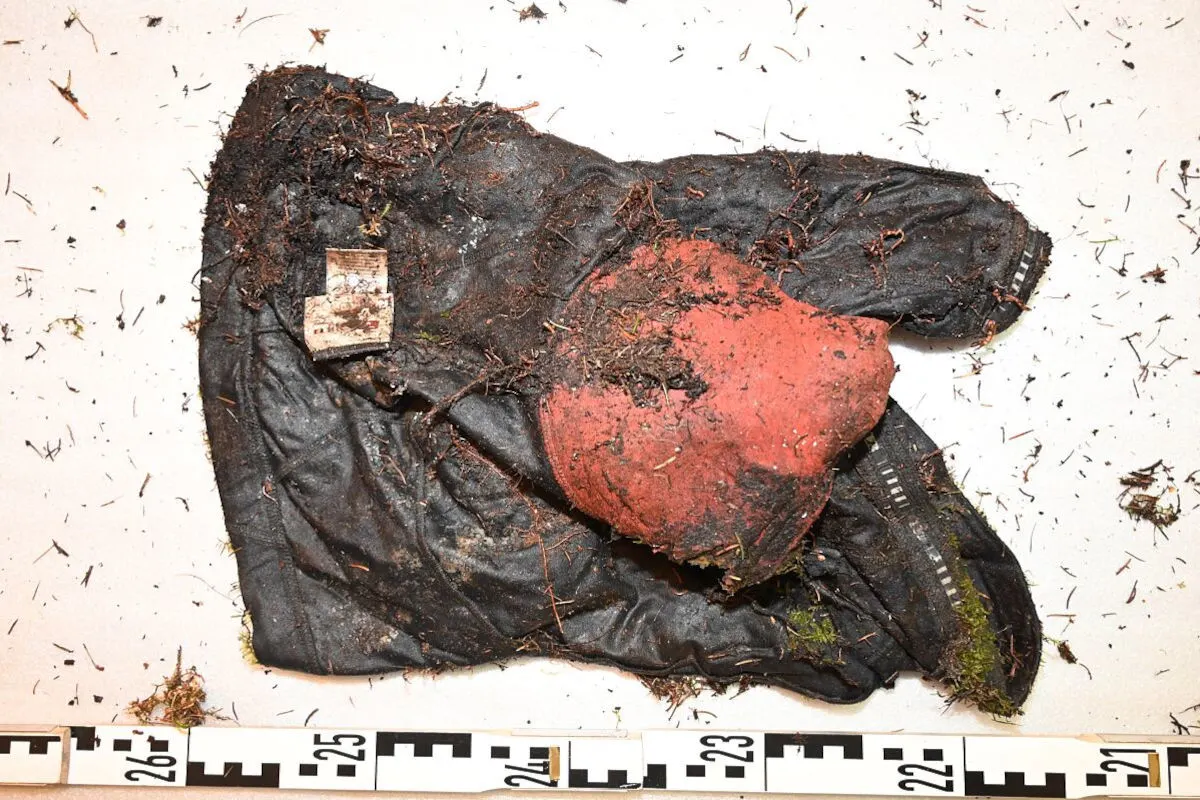 Ein schmutziger, schwarzer Handschuh mit roten Bereichen liegt auf einem hellen Untergrund. Eine Maßstabsleiste ist sichtbar.