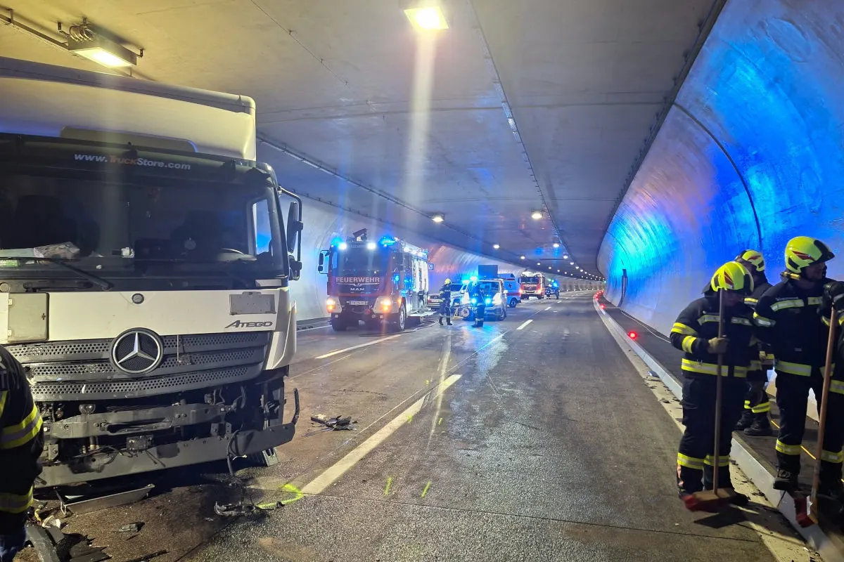 Ein beschädigter Lkw steht im Tunnel; Feuerwehrfahrzeuge und -leute sind im Einsatz. Der Tunnel ist von blauem Licht erleuchtet.