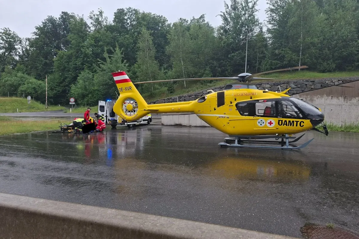 Ein gelber Rettungshubschrauber des ÖAMTC steht auf einer nassen Straße. Daneben versorgen Rettungskräfte eine Person.