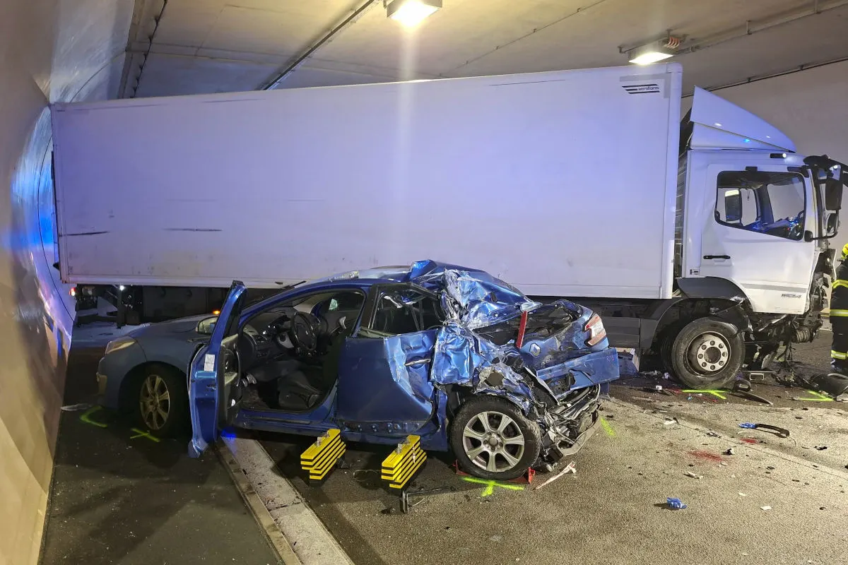 In einem Tunnel steht ein stark beschädigter blauer Pkw neben einem weißen Lkw. Der Pkw zeigt erhebliche Schäden auf der Beifahrerseite.
