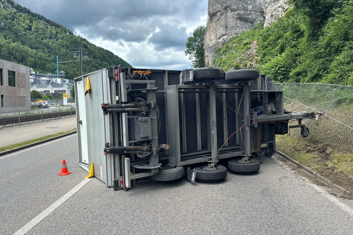 Ein umgestürzter Anhänger liegt auf der Seite und blockiert eine Straße. Im Hintergrund Felsen und Vegetation.