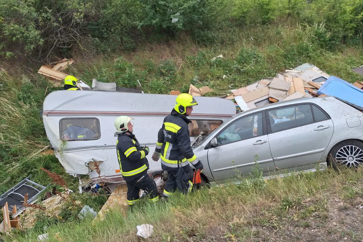 Zwei Feuerwehrleute in Schutzkleidung begutachten ein Auto, das in einen Wohnwagen auf einer Wiese gefahren ist.