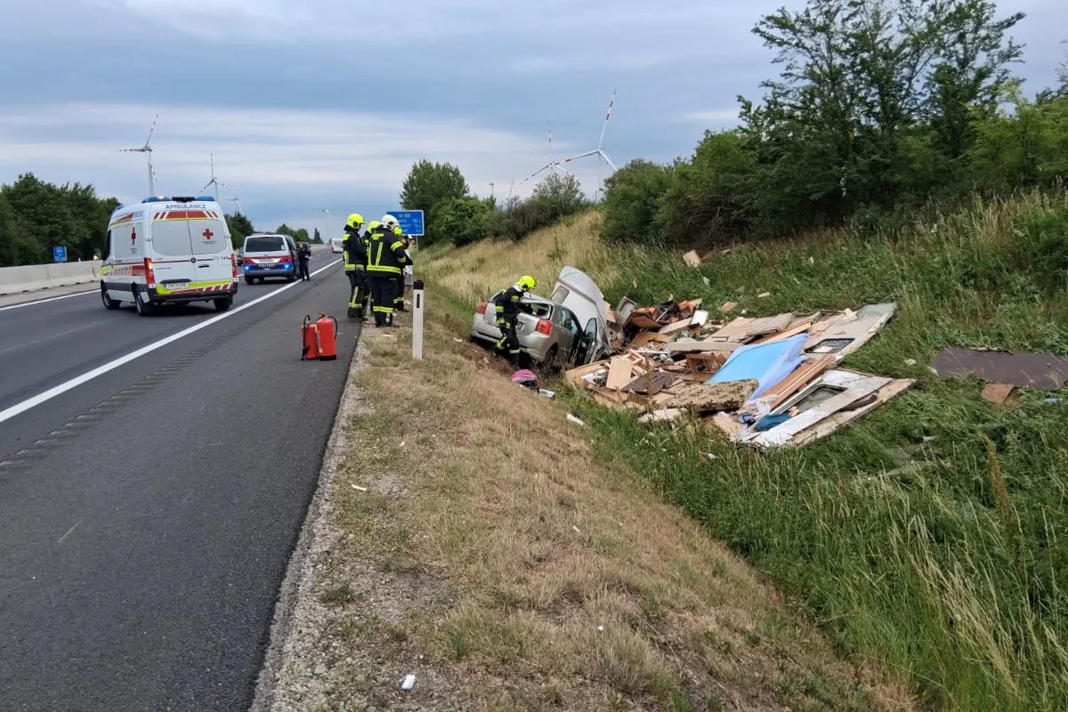 Ein Pkw liegt im Graben neben einer Autobahn, umgeben von Sperrmüll, während Rettungskräfte in gelber Schutzkleidung daneben stehen.