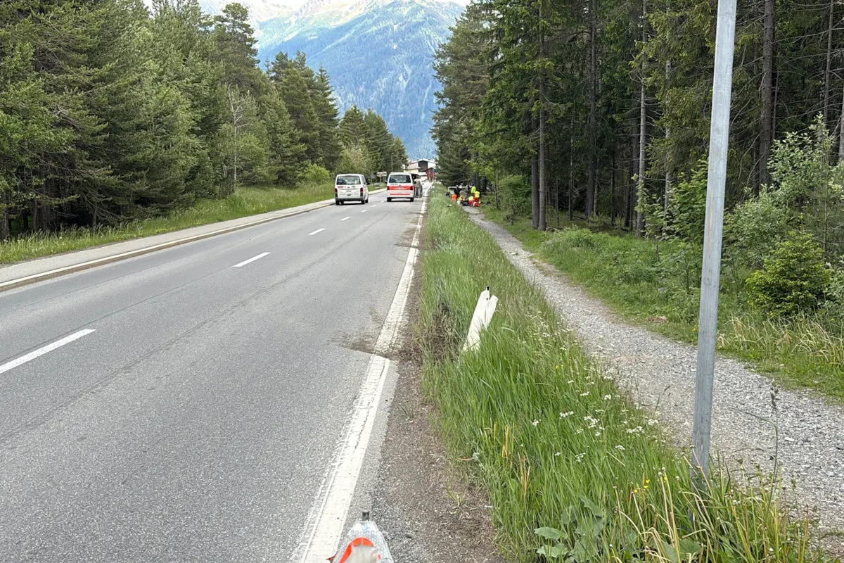 Zwei Vans stehen auf einer zweispurigen Straße, umgeben von einem Waldgebiet und Bergen im Hintergrund. Personen in Warnwesten sind neben der Straße sichtbar.