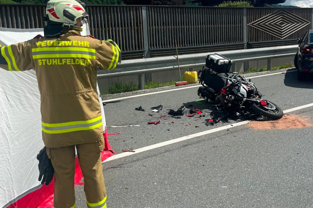 Ein Feuerwehrmann der Feuerwehr Stuhlfelden steht neben einem gestürzten Motorrad auf einer Straße. Trümmer liegen um das Motorrad verteilt.
