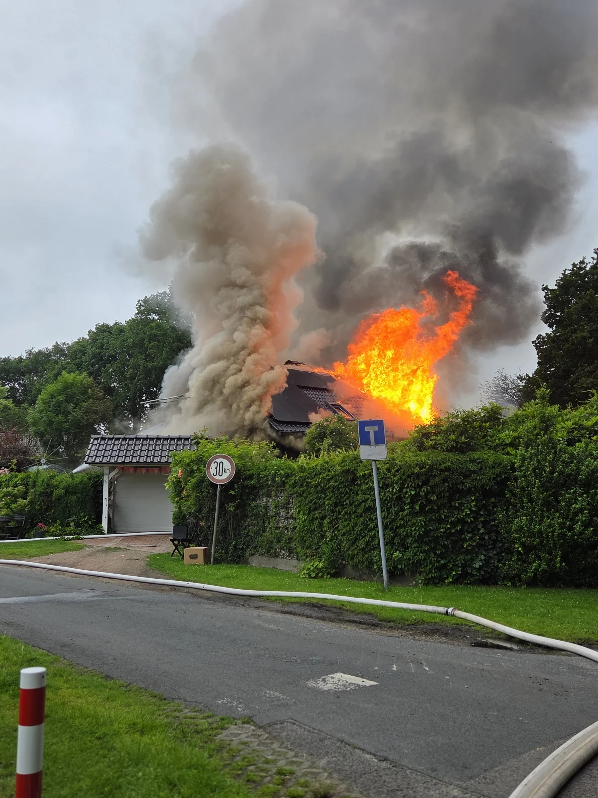 Ein intensives Feuer mit starken Flammen und Rauchentwicklung über einem Hausdach in einer Wohngegend.