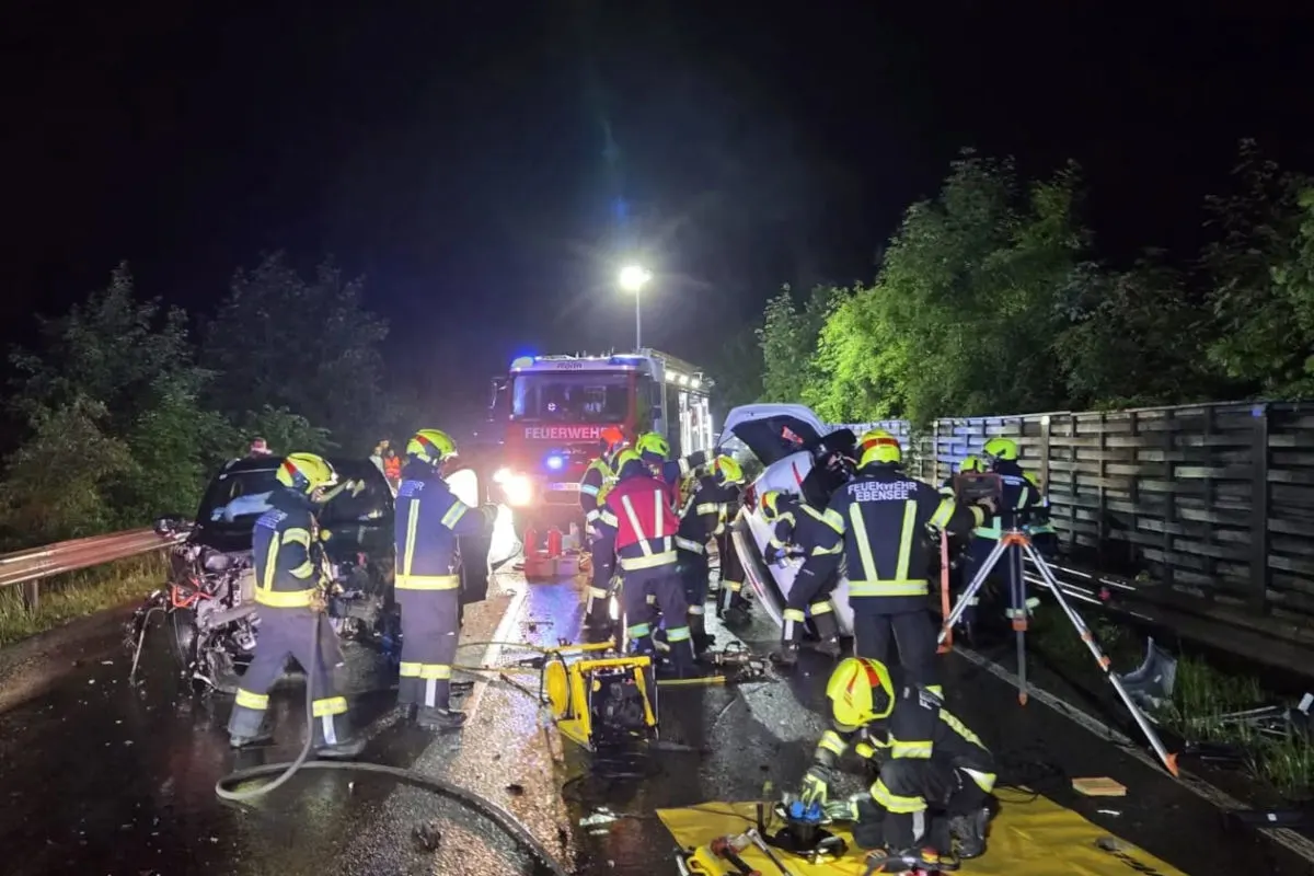 Mehrere Feuerwehrleute in Schutzkleidung arbeiten nachts an einem Unfallort. Ein Feuerwehrauto ist beleuchtet im Hintergrund.