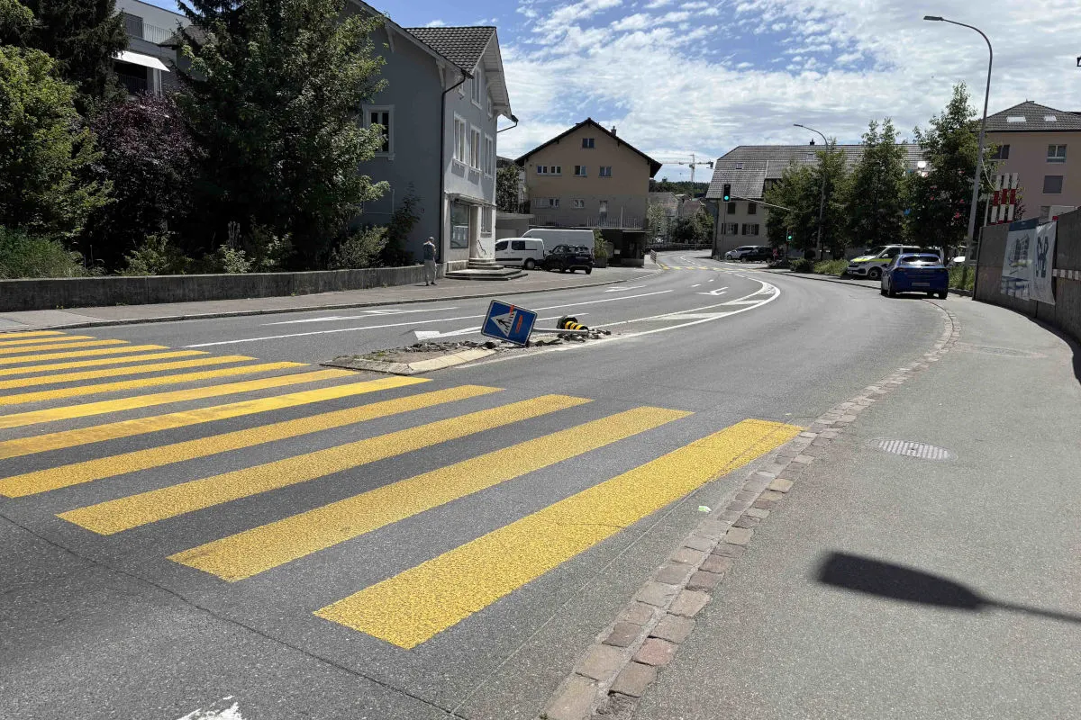 Ein Verkehrsschild liegt umgekippt auf einer Verkehrsinsel neben einer Kurve. Im Hintergrund sind Wohnhäuser zu sehen.