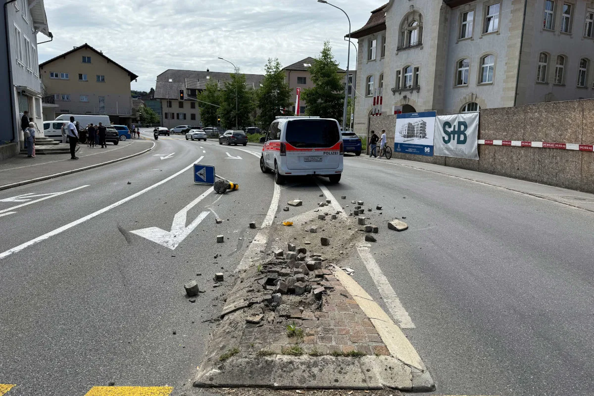 Eine Verkehrsinsel ist beschädigt, umgeben von Trümmern. Ein Polizeifahrzeug und Menschen stehen in der Nähe.