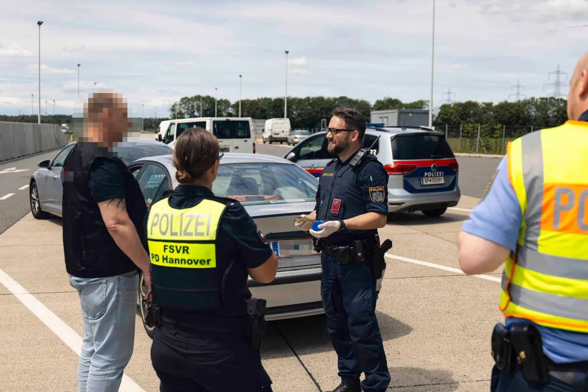 Mehrere Polizisten stehen bei einem Fahrzeug auf einem Autobahnrastplatz und sprechen mit einem Mann. Ein Polizeifahrzeug ist im Hintergrund zu sehen.