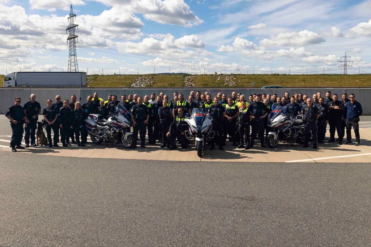Eine große Gruppe von Polizisten steht zusammen mit mehreren Motorrädern auf einer Autobahn bei Tageslicht.
