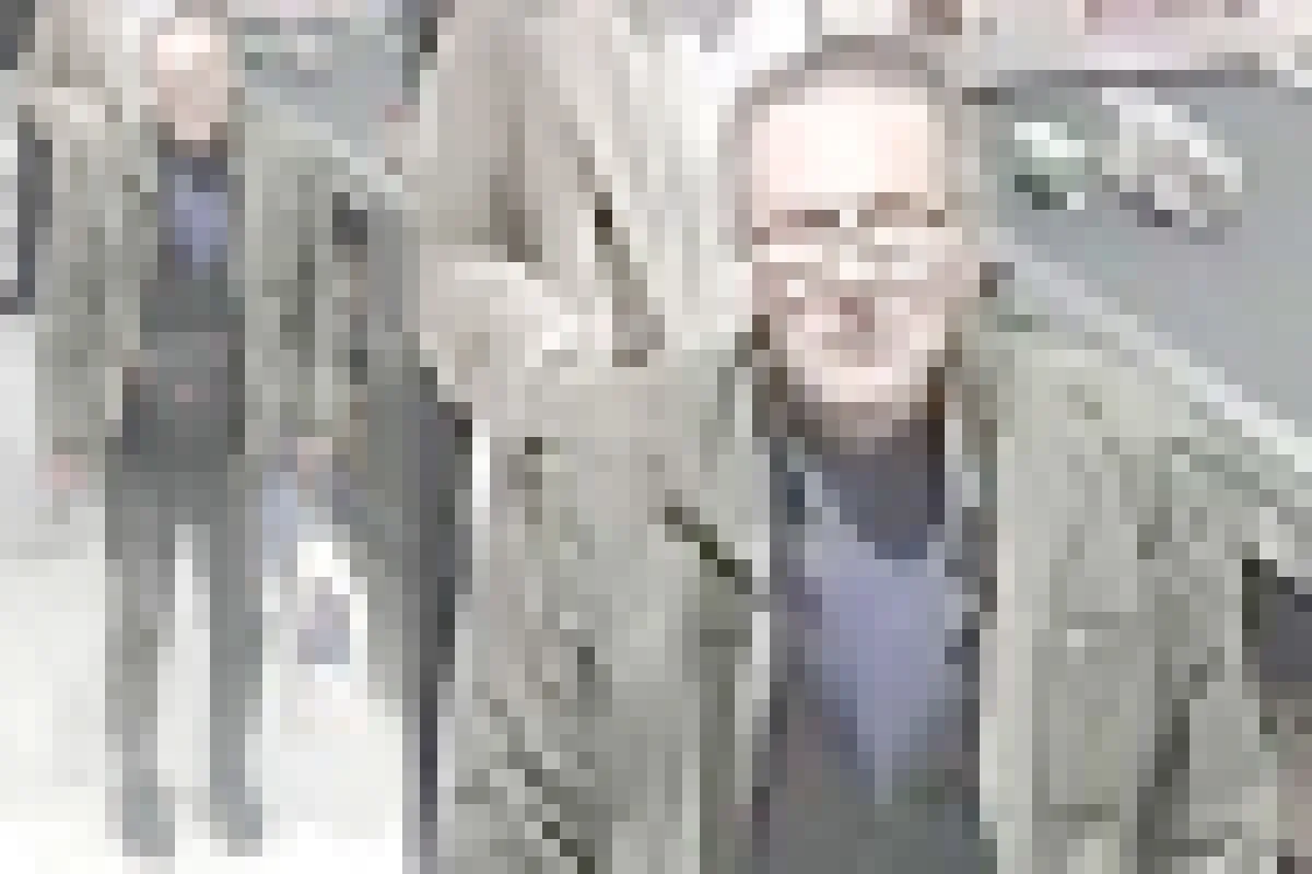 Ein Mann mit Brille und Winterjacke steht an einem Kassenschalter in einem Supermarkt. Er hält eine Einkaufstasche.