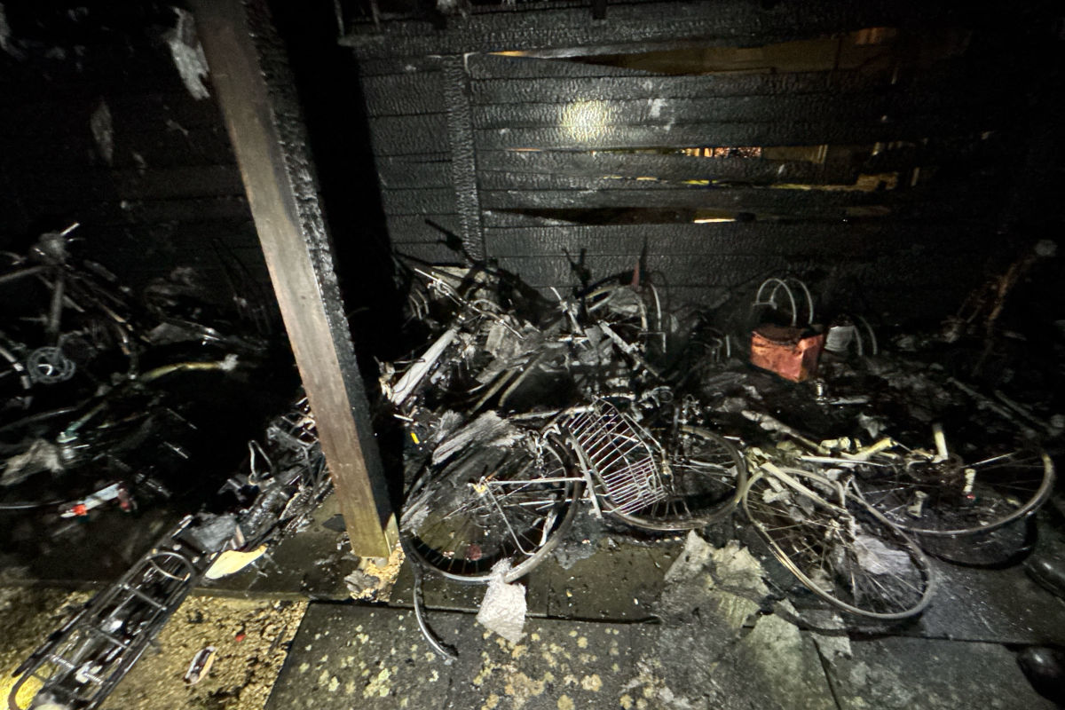 Mehrere verbrannte Fahrräder liegen in einem dunklen Raum, umgeben von Schutt und verbrannten Materialien.