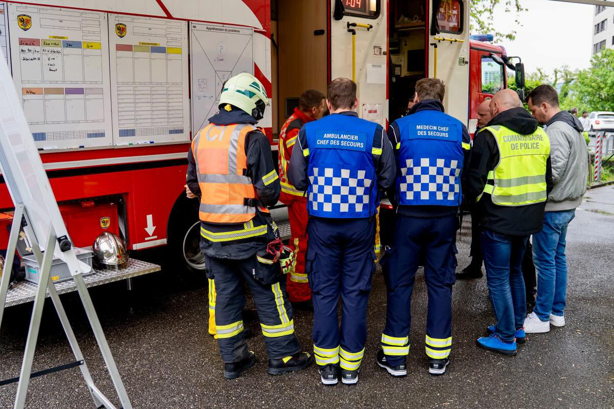 Eine Gruppe von Einsatzkräften in bunten Westen steht vor einem geöffneten Feuerwehrfahrzeug. Helme und Ausrüstungen sind sichtbar.