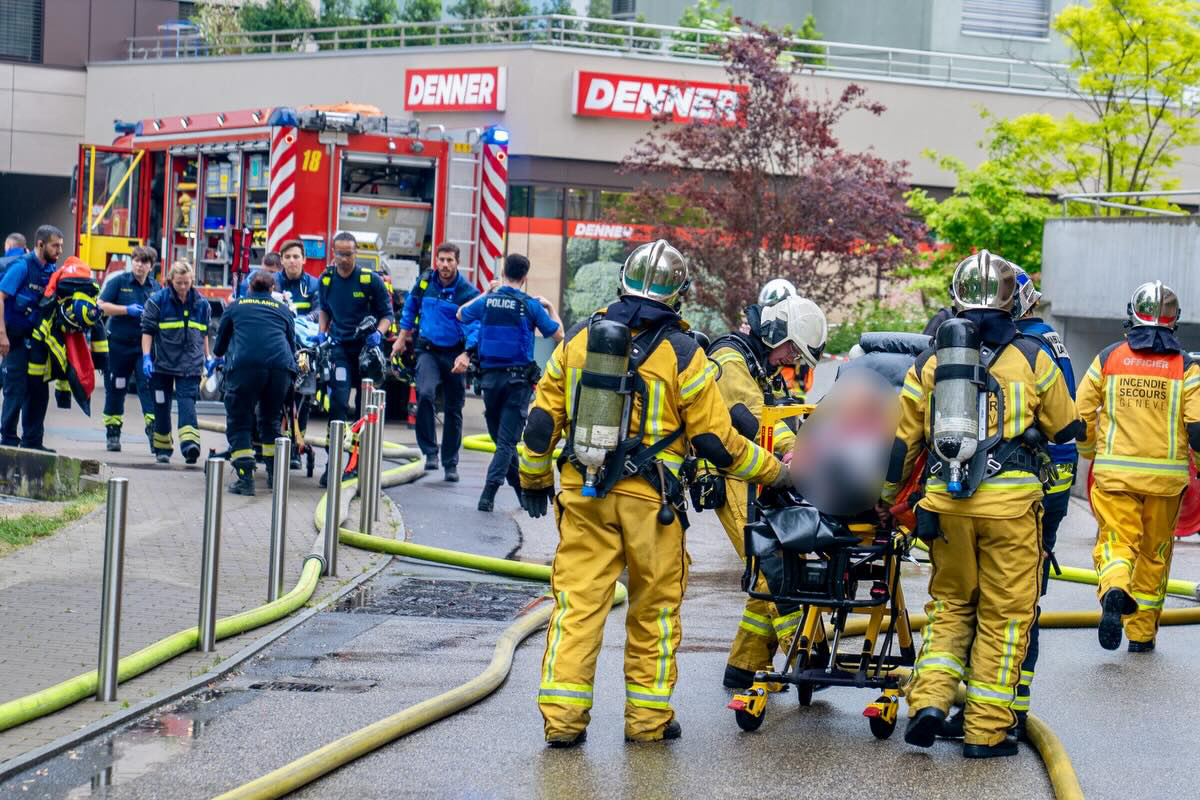 Mehrere Feuerwehrleute und Polizisten arbeiten bei einem Einsatz vor einem Geschäftsgebäude. Ein Feuerwehrwagen ist im Hintergrund sichtbar.