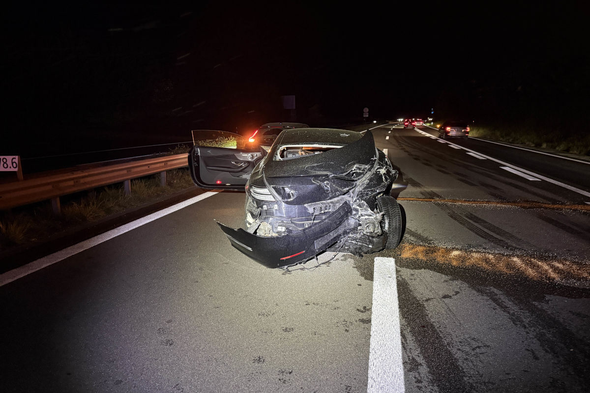 Ein stark beschädigtes Auto steht auf einer Autobahn. Die Front ist stark eingedrückt, und die Szene ist bei Nacht aufgenommen.