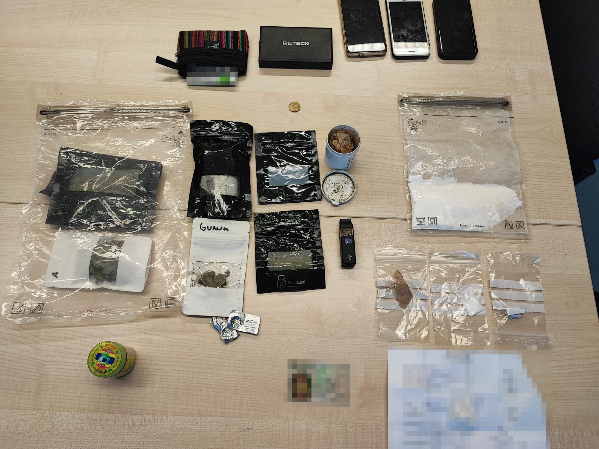 Mehrere beschlagnahmte Gegenstände inklusive Beutel und Verpackungen liegen geordnet auf einem Tisch. Elektronik ist ebenfalls zu sehen.