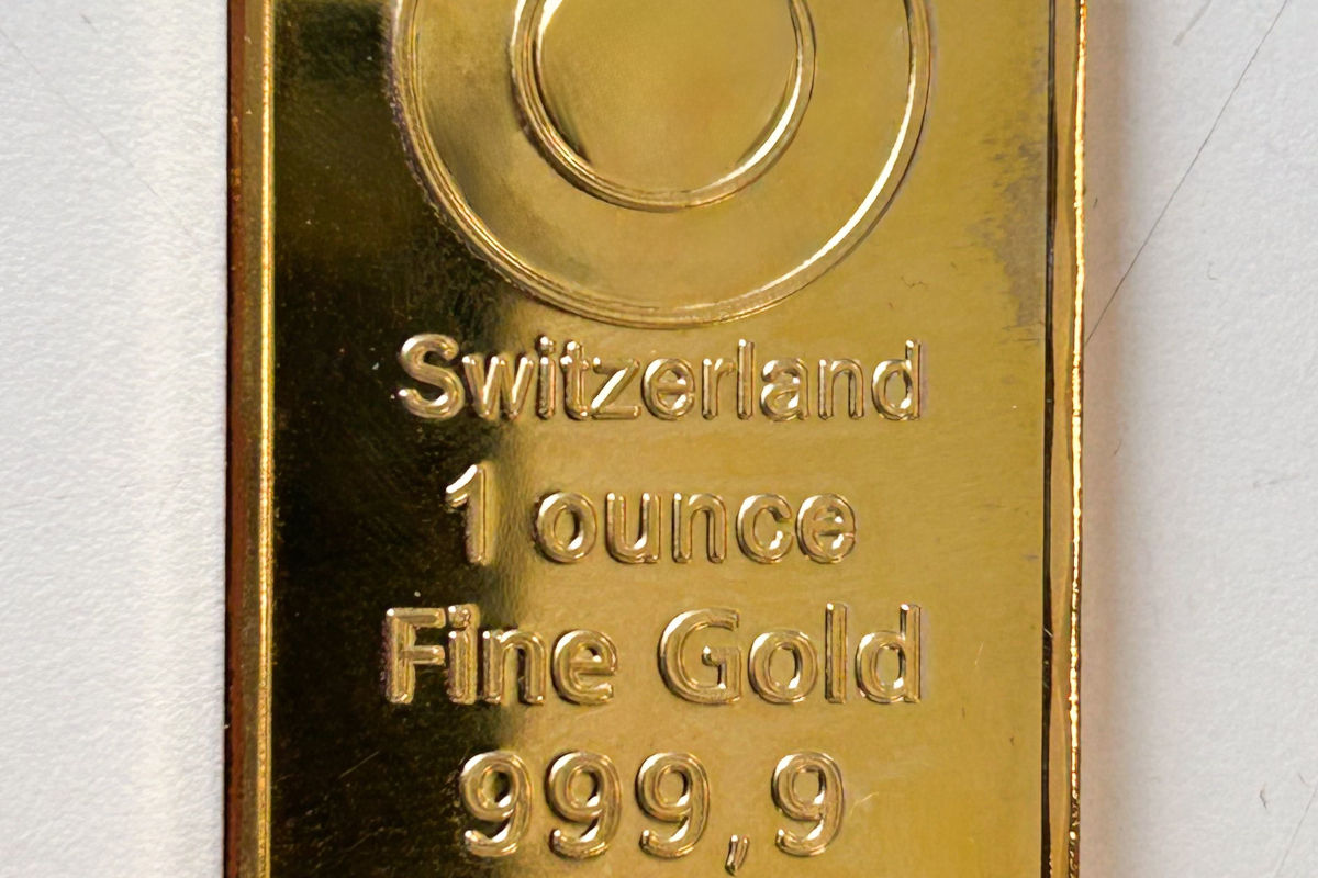 Ein nahaufgenommener Goldbarren mit der Aufschrift 'Switzerland, 1 ounce, Fine Gold, 999,9'. Der Barren hat einen glänzenden goldenen Farbton.