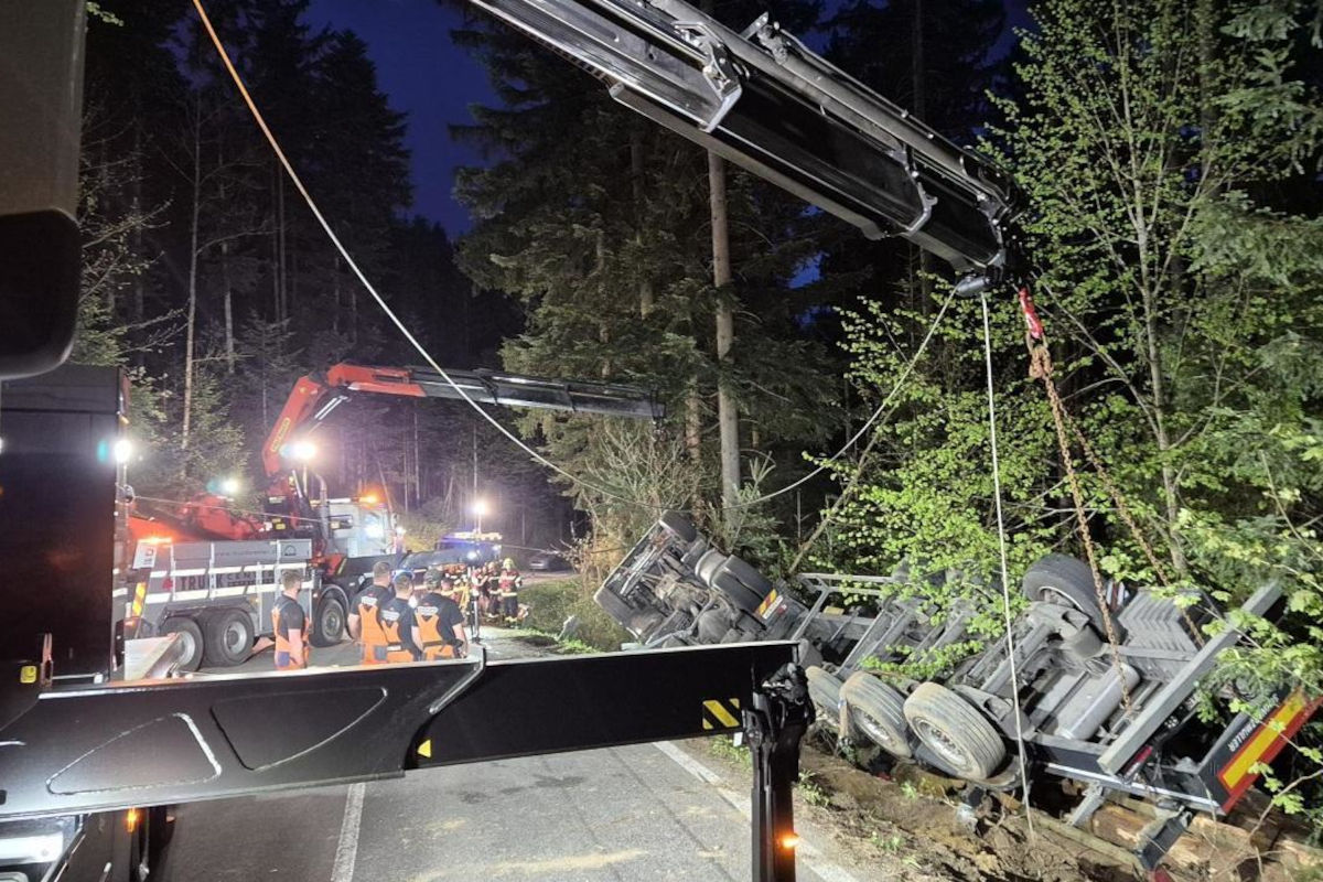 In einem Waldgebiet wird bei Nacht ein Lastwagen von zwei Kränen angehoben. Mehrere Einsatzkräfte mit Warnwesten sind vor Ort.