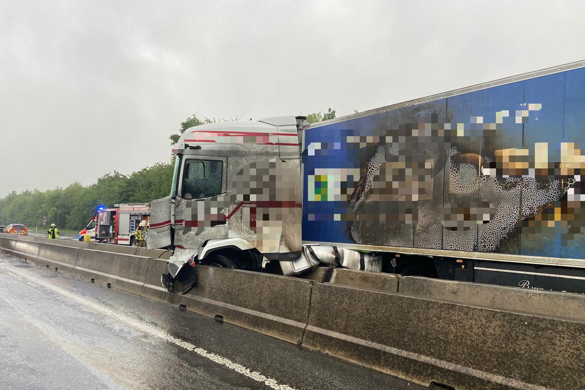 Ein LKW mit deutlichen Schäden an der Front steht auf einer Autobahn. Der Himmel ist bewölkt und die Straße ist nass.