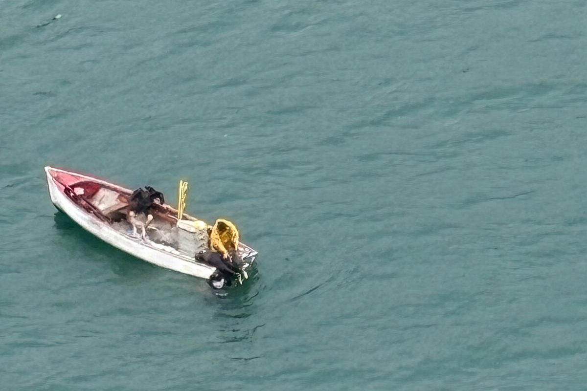 Ein kleines, baufälliges Boot befindet sich inmitten eines Gewässers. Zwei Personen und einige Gegenstände sind an Bord sichtbar.
