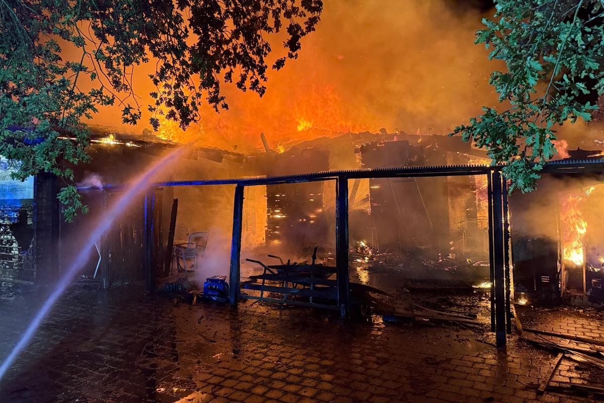 Ein Gebäude steht bei Nacht in Flammen, mit Feuerwehrleuten, die den Brand bekämpfen. Rauch steigt vom Dach auf.
