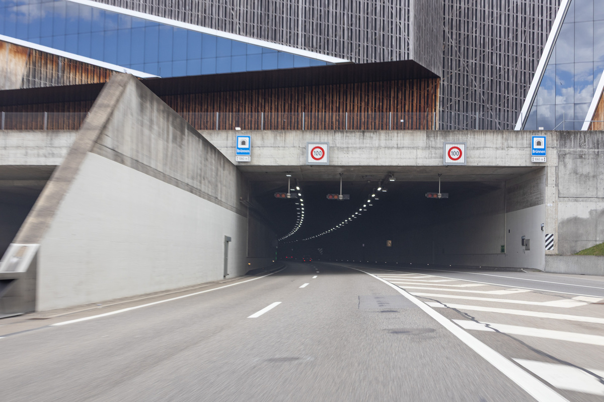 Die Aufnahme zeigt die Einfahrt eines Autobahntunnels mit Verkehrsschildern, die eine Geschwindigkeitsbegrenzung anzeigen. Im Hintergrund sind Beleuchtungen innerhalb des Tunnels sichtbar.