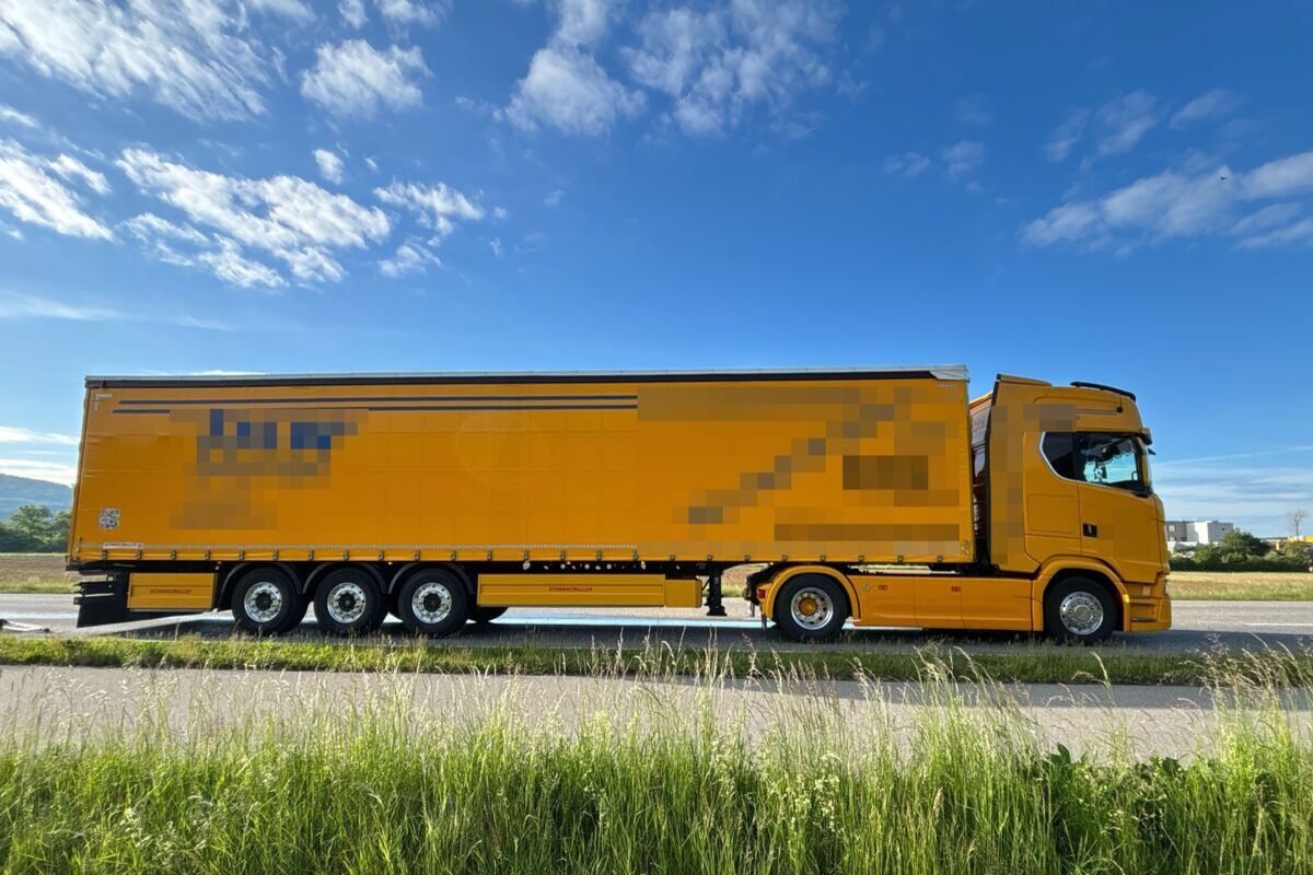 Großer gelber Lastwagen parkt auf einer Landstraße bei klarem Himmel.