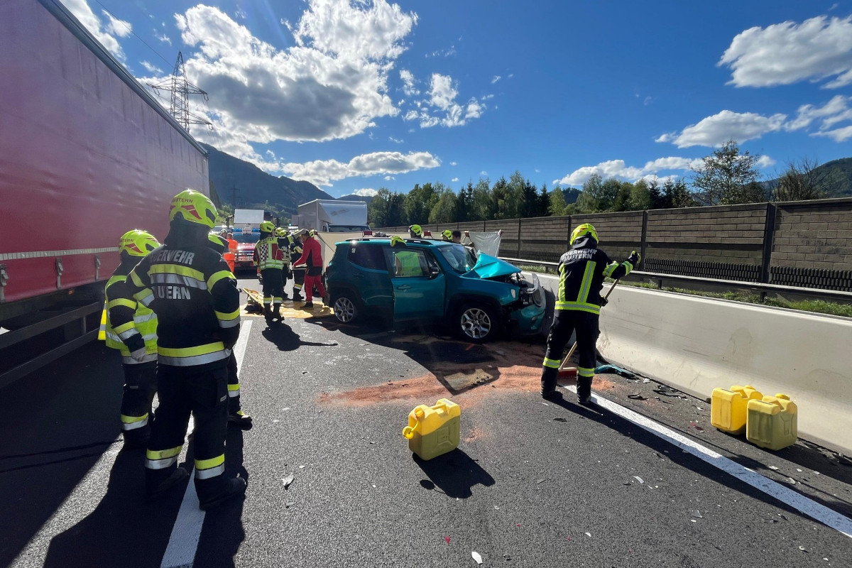 Ein blauer SUV ist in einen Unfall auf der Autobahn verwickelt. Feuerwehrleute in gelb-schwarzen Uniformen arbeiten an der Unfallstelle.