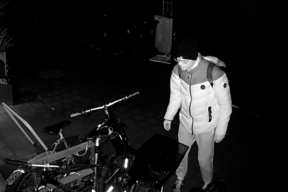 Eine Person mit einer warmen Jacke und Mütze steht neben mehreren Fahrrädern. Die Szene ist dunkel, möglicherweise nachts.