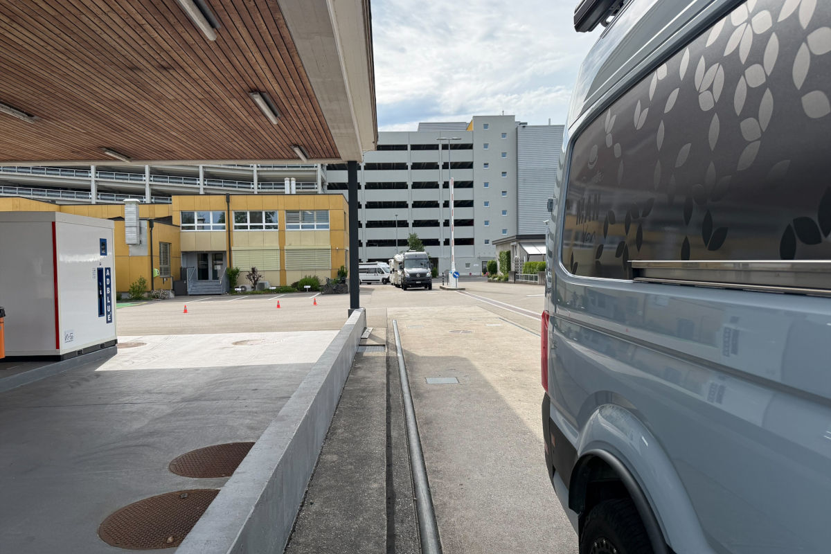 Ein geparkter Transporter auf einem Parkplatz nahe eines Gebäudekomplexes.