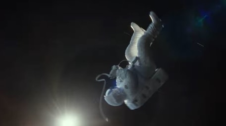 Szene aus "Gravity". Sandra Bullock treibt als Astronautin Kopfüber durch die Leere des Weltalls, unten links leuchtet die Sonne.