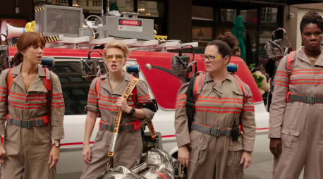 Die vier weiblichen Ghosbusters aus dem Film von 2014 in voller Montur vor dem Ghostbusters-Mobil stehend