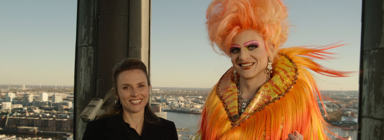 Die junge Pastorin (Karin Hanczewski) und Olivia Jones (Johannes Hegemann) stehen auf dem Hamburger Michel nebeneinander und lächeln freundlich in die Kamera.