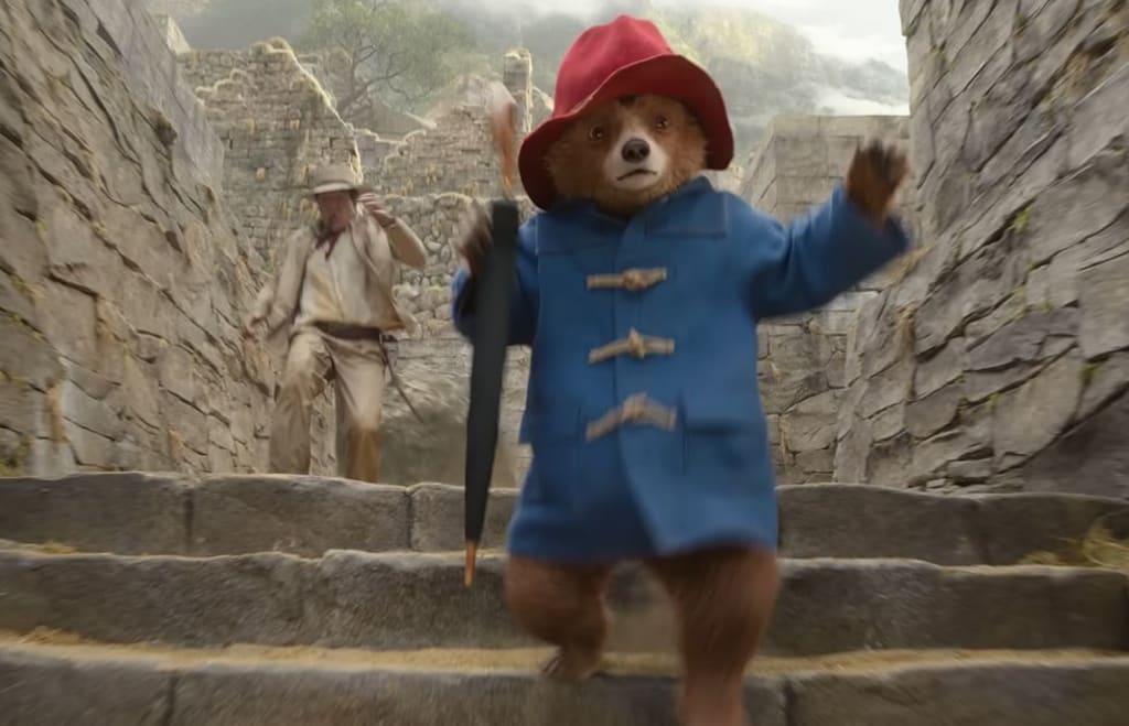 Szene aus "Paddington in Peru". Im Vordergrund rennt Paddington eine Steintreppe in Ruinen heraunter, gefolgt von Antonio Banderas im Abenteueroutfit und einer Indiana-Jones-mäßigen Steinkugel