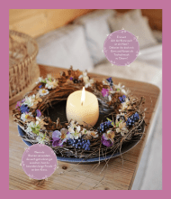 Das Bild zeigt einen Kranz aus Naturmaterialien auf einem Teller. In der Mitte des Kranzes steht eine angezündete Kerze