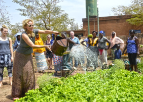 Katja Riemann gießt ein Pflanzenbeet, die Bewohner des Frauenhauses in Burkina Faso sehen zu