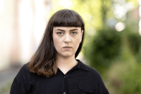 Porträt der Autorin Anna Yeliz Schentke. Sie steht in einer schwarzen Bluse vor einem unscharfen Hintergrund und schaut direkt in die Kamera.